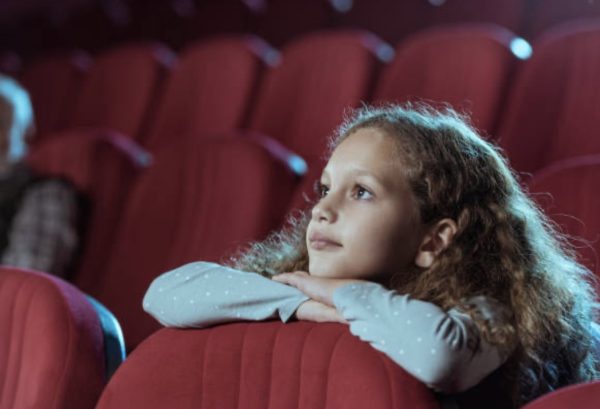 The photo is mainly focused on a young girl who is watching a movie in the theaters. Movies often teach valuable lessons through breath taking stories that make it hard for you to take your eyes off of the screen.